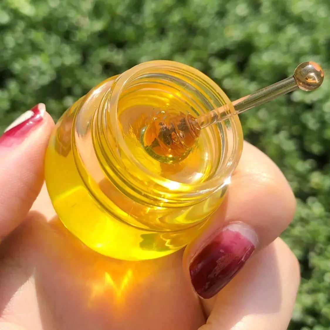 Hand holding a small jar of golden lip treatment with a spatula, perfect for nourishing dry lips.